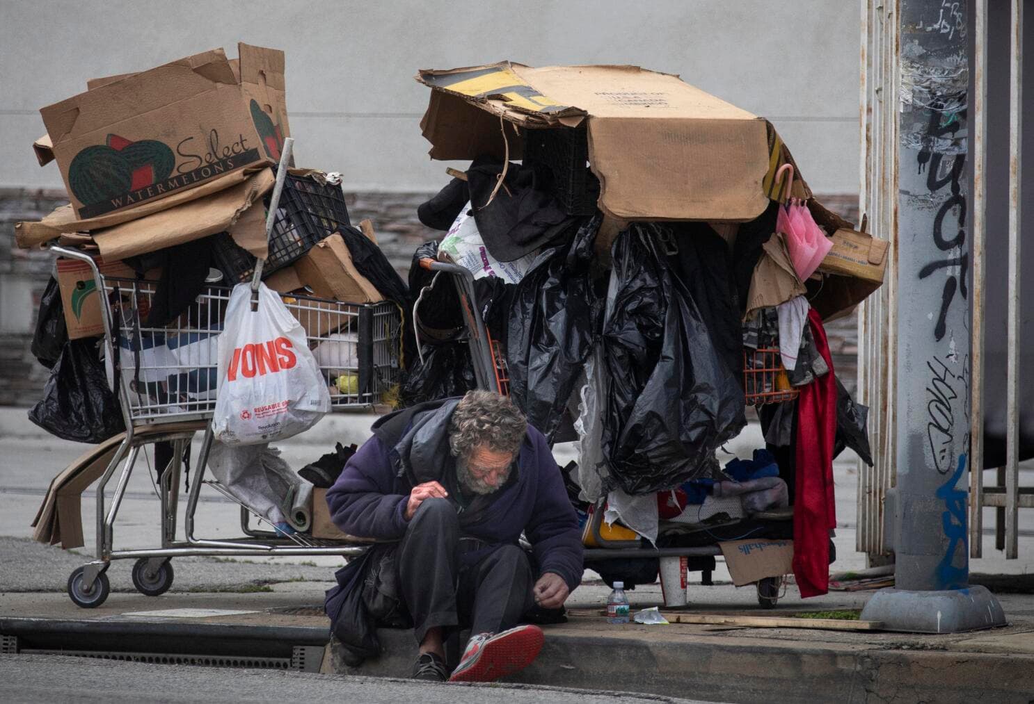 A person sitting near belongings on a city sidewalk.